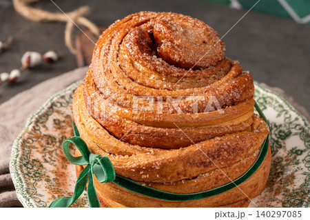 Close-up of a flaky puff pastry Easter bread coated in cinnamon sugar and tied with a green velvet ribbon on a vintage plate with rustic spring decor 140297085