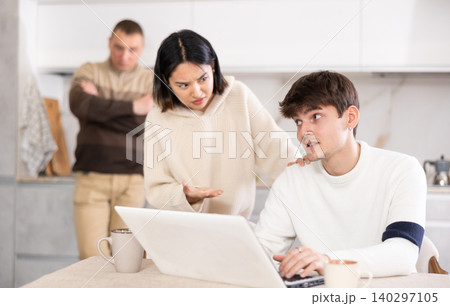 Girl persuades a young guy to stop playing computer games. Upset father in background Girl persuades a young guy to stop playing computer games. Upset father in background 140297105