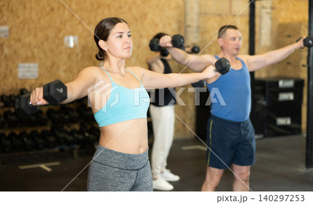 Sporty young woman performing exercises with dumbbells in gym 140297253