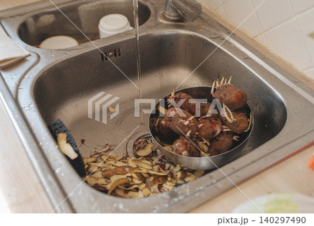 Peeling raw potatoes in a kitchen sink Peeling raw potatoes in a kitchen sink 140297490