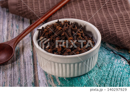 Aromatic whole dried cloves in white ceramic bowl on rustic wooden background 140297929