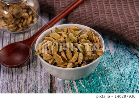 Aromatic green cardamom pods in white bowl on rustic turquoise wooden table with spoon and jar 140297930