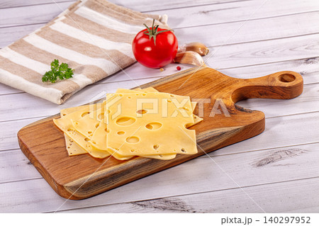 Sliced Swiss cheese on wooden cutting board with fresh tomato and garlic Sliced Swiss cheese on wooden cutting board with fresh tomato and garlic 140297952