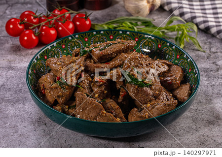 Sauteed pork liver with garlic, chili and herbs in decorative green bowl on gray table 140297971