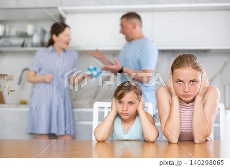 Upset teenage girls sitting in kitchen while parents quarreling 140298065