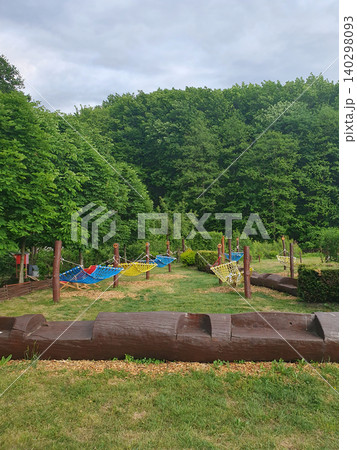 Cozy outdoor recreation area with bright hammocks and wooden benches against the backdrop of a dense green forest Cozy outdoor recreation area with bright hammocks and wooden benches against the backdrop of a dense green forest 140298093
