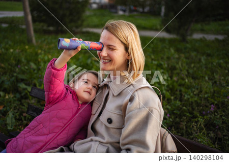 Mother and daughter playing with kaleidoscope on park bench Mother and daughter playing with kaleidoscope on park bench 140298104