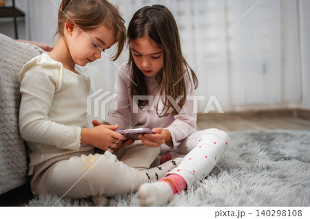 Children sisters bonding playing on smartphone at home Children sisters bonding playing on smartphone at home 140298108
