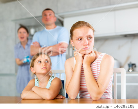 Frightened and frowning children sit at kitchen table during mom and dad quarrel 140298109