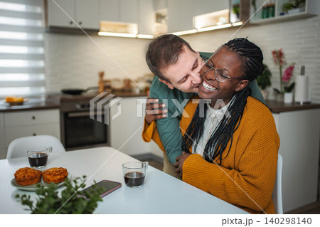 Interracial couple sharing tender kiss at kitchen table Interracial couple sharing tender kiss at kitchen table 140298140