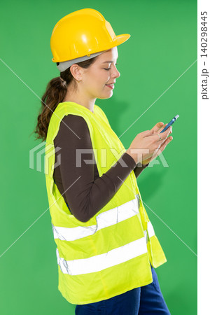 Young woman in reflective vest and hard hat scrolling smartphone Young woman in reflective vest and hard hat scrolling smartphone 140298445