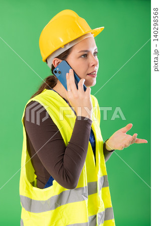 Young woman wearing reflective vest and hardhat talking on smartphone 140298568