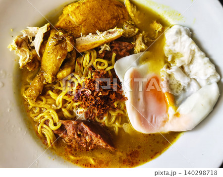 Close up of a bowl of hot Indonesian instant noodle soup with chicken, a soft-boiled egg, and crispy fried shallots. Close up of a bowl of hot Indonesian instant noodle soup with chicken, a soft-boiled egg, and crispy fried shallots. 140298718