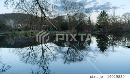 Bare Trees Reflected In Calm Blue Water Bare Trees Reflected In Calm Blue Water 140298894