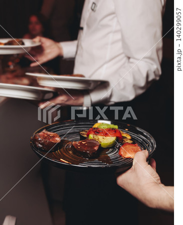Waiter in uniform serving dishes and drinks on party, server carrying plates with food and beverages at the table, catering service on wedding reception, personnel in cafe restaurant, staff on event Waiter in uniform serving dishes and drinks on party, server carrying plates with food and beverages at the table, catering service on wedding reception, personnel in cafe restaurant, staff on event 140299057