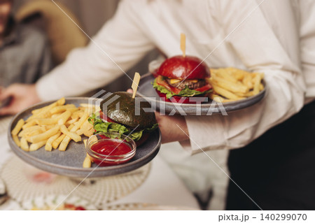 Waiter in uniform serving dishes and drinks on party, server carrying plates with food and beverages at the table, catering service on wedding reception, personnel in cafe restaurant, staff on event 140299070