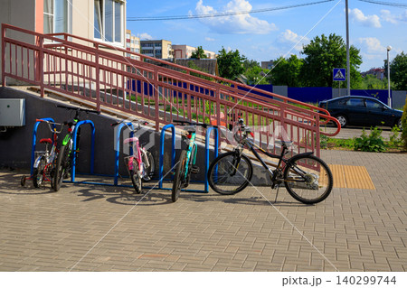 Bicycles parked at blue metal rack near building ramp, children and adult bikes on urban street sidewalk Bicycles parked at blue metal rack near building ramp, children and adult bikes on urban street sidewalk 140299744