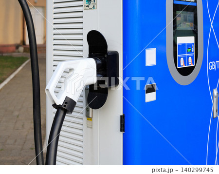 White EV charger handle plugged into blue terminal, public electric vehicle station interface panel closeup White EV charger handle plugged into blue terminal, public electric vehicle station interface panel closeup 140299745