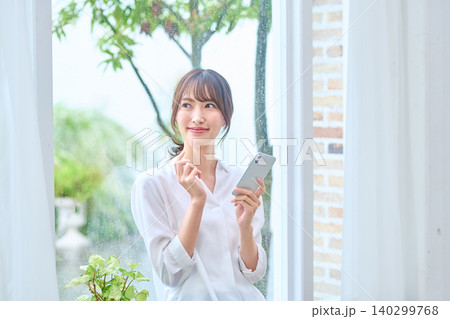 スマホを手に窓の外を見る女性 140299768