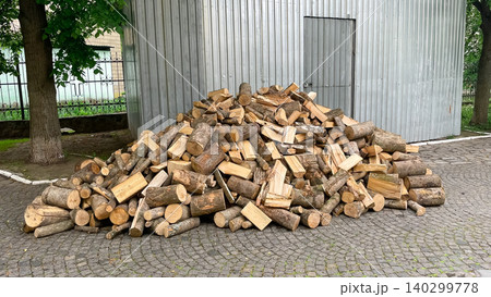 Large pile of chopped firewood on pavement near a metal building 140299778