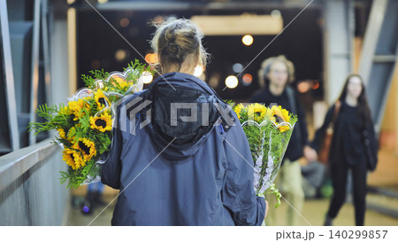 Woman carrying sunflowers on an urban pedestrian bridge at night, walking with gifts 140299857