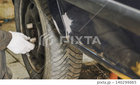 Hand in glove tightening lug nuts on a car wheel, performing maintenance and repair 140299865