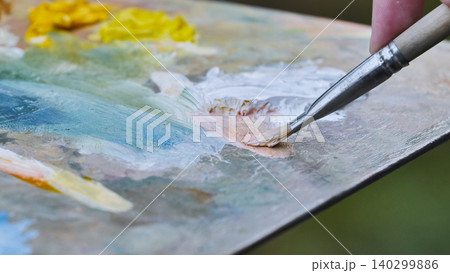 Artist mixing oil paints on palette with brush creating new color 140299886