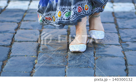 Indian woman walking on cobblestone street wearing traditional sari and shoes 140300132