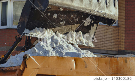 Excavator loading snow from street into truck during winter snow removal operation 140300186