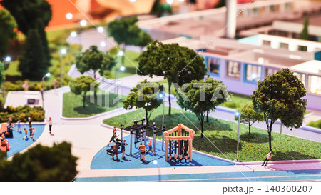 Miniature public park model with people enjoying playground and city lights at night 140300207