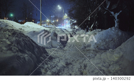 Winter night in a city with snowdrifts flanking a cleared pedestrian pathway Winter night in a city with snowdrifts flanking a cleared pedestrian pathway 140300292