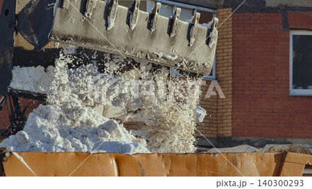 Excavator bucket dumping snow into truck, clearing urban street after harsh winter Excavator bucket dumping snow into truck, clearing urban street after harsh winter 140300293
