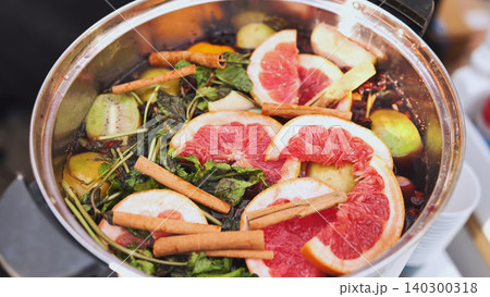 Warm mulled wine preparing with grapefruit slices, cinnamon sticks, and mint in a pot 140300318