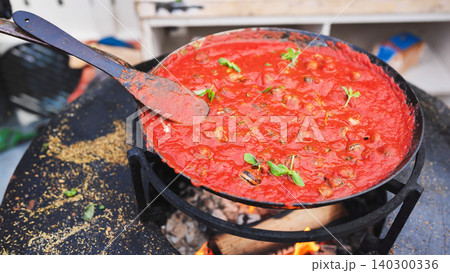 Snails cooking in tomato sauce over open fire 140300336