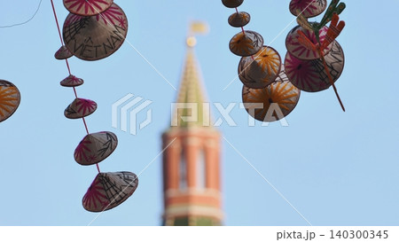 Traditional Vietnamese conical hat decorations hanging at an outdoor festival with a blurred historic tower in the background. Traditional Vietnamese conical hat decorations hanging at an outdoor festival with a blurred historic tower in the background. 140300345