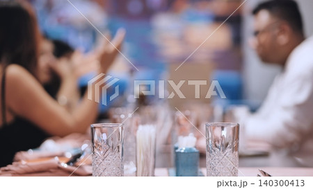 Dinner table setting with glassware and blurred people enjoying social gathering Dinner table setting with glassware and blurred people enjoying social gathering 140300413