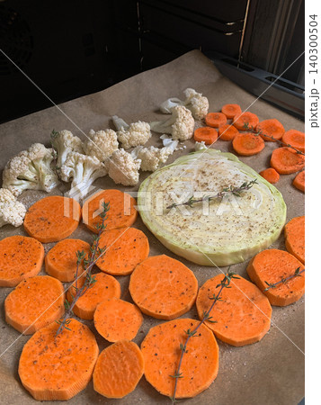 Vegetables including sweet potato with cabbage and cauliflower are prepared on a baking tray ready to bake in the oven. The tray is lined and set on a stove surface Vegetables including sweet potato with cabbage and cauliflower are prepared on a baking tray ready to bake in the oven. The tray is lined and set on a stove surface 140300504