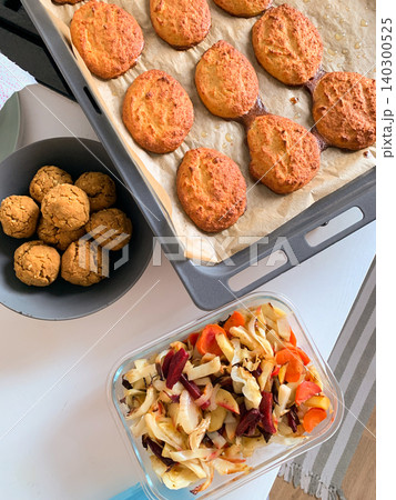 Lentil pancakes and chickpea buns are arranged on a baking tray. A bowl of baked vegetables sits on the table. This scene takes place in a cozy kitchen setting Lentil pancakes and chickpea buns are arranged on a baking tray. A bowl of baked vegetables sits on the table. This scene takes place in a cozy kitchen setting 140300525