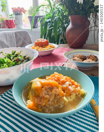 Cabbage rolls filled with meat and grains sit in a blue bowl. The dish is covered in a rich tomato sauce. It is ready to be enjoyed at dinner time in a warm kitchen Cabbage rolls filled with meat and grains sit in a blue bowl. The dish is covered in a rich tomato sauce. It is ready to be enjoyed at dinner time in a warm kitchen 140300537