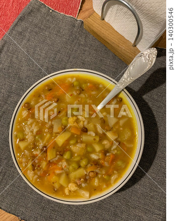 A bowl of potato rice soup holds a mix of carrots and green peas. This dish sits on a cozy table with simple tableware. It is a hearty meal perfect for comfort food lovers A bowl of potato rice soup holds a mix of carrots and green peas. This dish sits on a cozy table with simple tableware. It is a hearty meal perfect for comfort food lovers 140300546