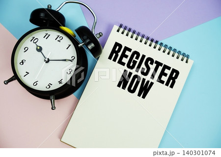 Register Now text written on notepad with alarm clock flat lay on multicolor pastel background 140301074