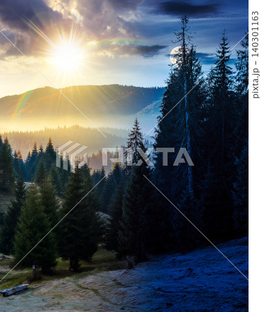 day meet night. cold fog in the mountain valley. nature phenomenon over epic mountain landscape with coniferous forest. sun and moon over spruce trees in misty nature background view from a hill 140301163