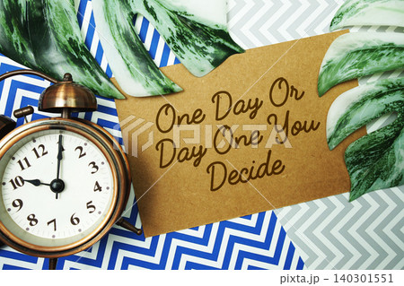 One Day Or Day One. You Decide text with alarm clock and monstera leave on blue background One Day Or Day One. You Decide text with alarm clock and monstera leave on blue background 140301551