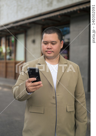 Plus size Isan Thai businessman using phone outside an urban building Plus size Isan Thai businessman using phone outside an urban building 140302091