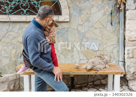 Dad and daughter family look cute fluffy cat, man and girl walk outside with pet 140302326