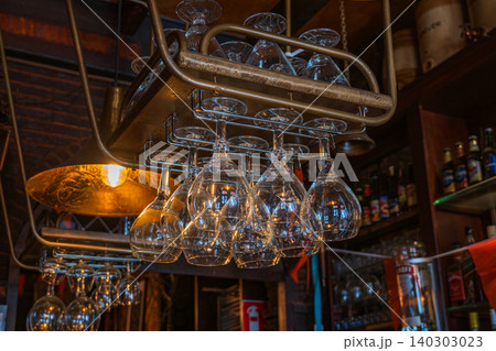 Amsterdam, Netherlands, 22.04.2026 - Wine glasses hanging on rack over a bar counter in a traditional dutch pub interior in zaandam, cozy warm light illumination in restaurant evening atmosphere Amsterdam, Netherlands, 22.04.2026 - Wine glasses hanging on rack over a bar counter in a traditional dutch pub interior in zaandam, cozy warm light illumination in restaurant evening atmosphere 140303023