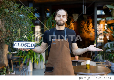 Disappointed waiter holding closed sign and shrugging Disappointed waiter holding closed sign and shrugging 140303273