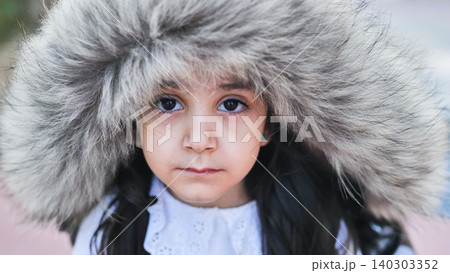 Little girl wearing a warm fur hood, looking at camera and embracing winter season Little girl wearing a warm fur hood, looking at camera and embracing winter season 140303352