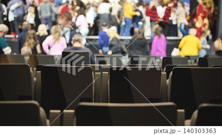 Rows of empty seats in a venue with blurred people dancing in the background 140303363