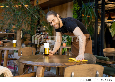 Smiling staff member sanitizing table surface 140303435